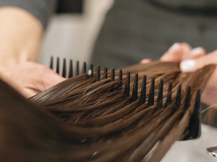 Frisör som kammar igenom långt brunt hår med en tunn kam